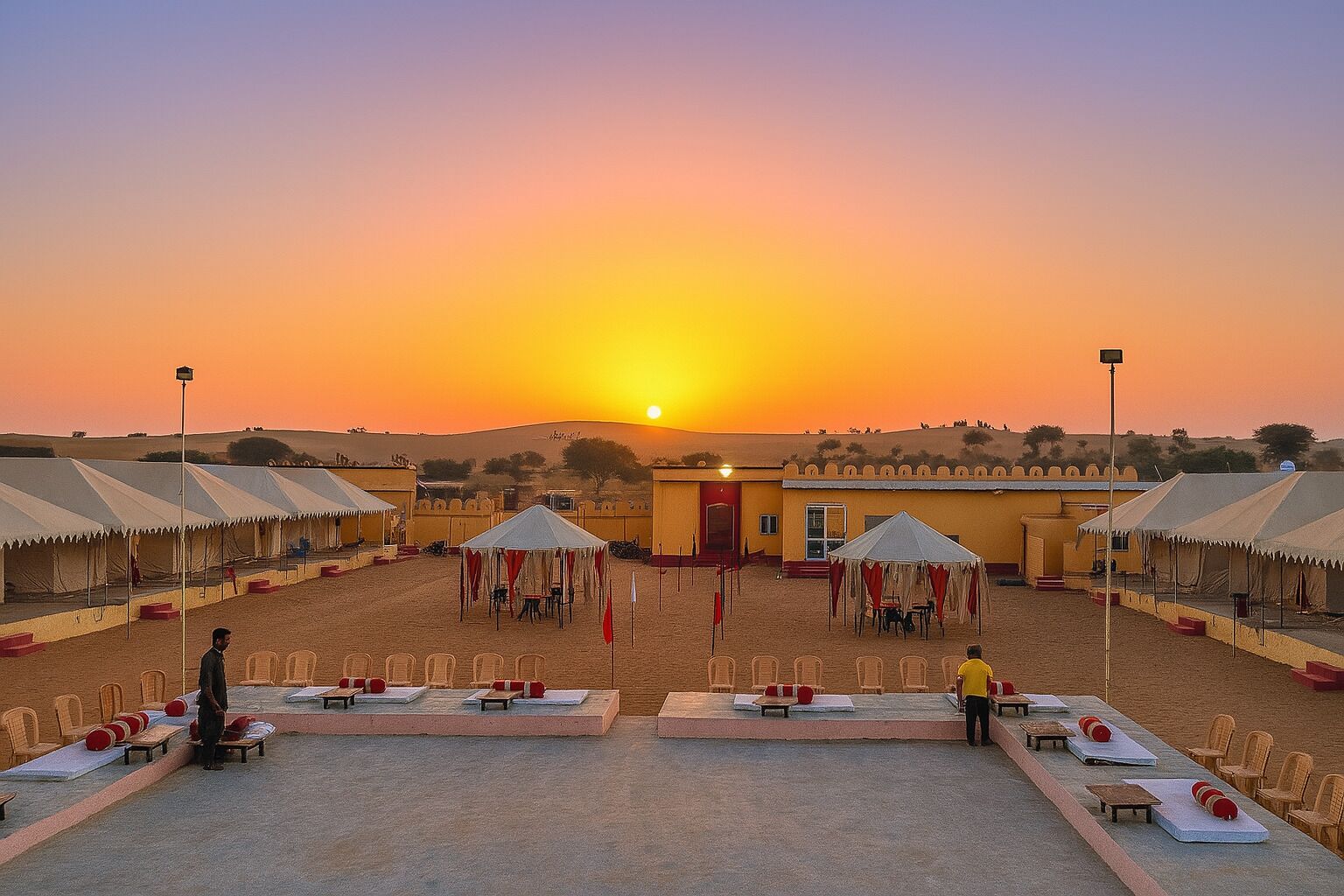 Un complexe hôtelier situé dans le désert, avec des tentes et un espace dédié aux repas, le tout baigné par les couleurs du coucher de soleil.