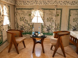 Una habitación con dos sillas de madera, una mesita redonda con una bandeja y una cama.