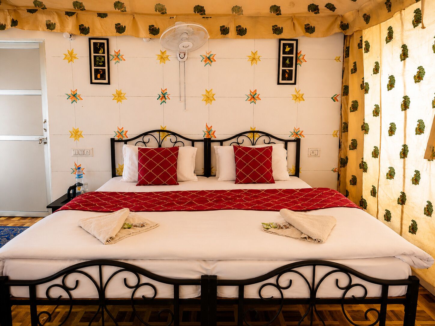 A bed with a red and white bedspread, two pillows, a bedside table with a water bottle, and a fan on the ceiling.