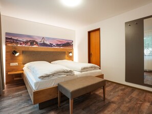 Ein ordentlich bezogenes Bett mit einem Holzkopfteil, einem Nachttisch und einer Bank.