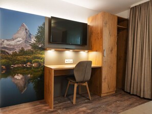 Een hotelkamer met een houten bureau, een stoel, een televisie boven het bureau en een schilderachtige muurschildering.