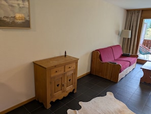 Ein Zimmer mit einem Holzschrank, einem rosafarbenen Sofa, einem Kuhfellteppich und einem Gemälde an der Wand.