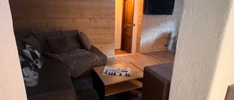 Un espacio habitable compacto con un sofá, una mesa de centro y un televisor pequeño montado en la pared.
