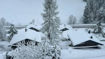 A snow-covered landscape with two cabins and a forest in the background.