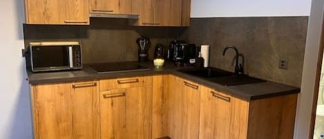 A compact kitchen with wooden cabinets, a microwave, a coffee maker, and a sink.