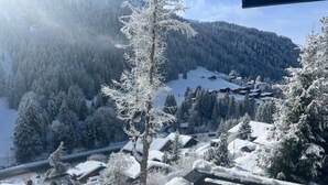 Un village enneigé, avec des bâtiments et des arbres, une clôture en bois et une montagne en arrière-plan.
