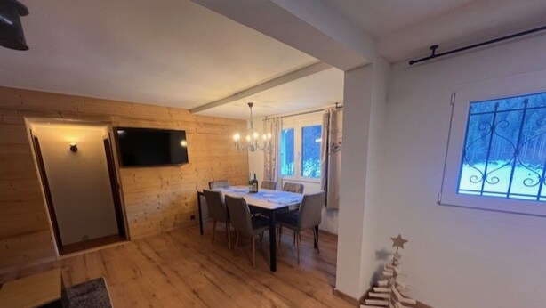 Une pièce dotée d’un plancher en bois, d’une table à manger avec des chaises, d’un téléviseur fixé au mur et d’une fenêtre ornée d’une grille décorative.
