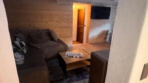 Une pièce chaleureuse avec un plancher en bois, un canapé, une table basse et une porte qui donne sur une autre pièce.