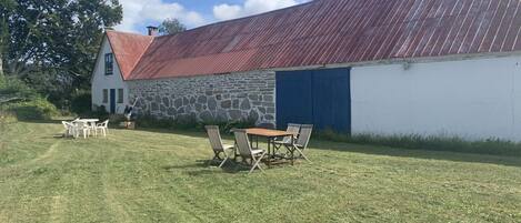 A stone building with a red roof, a white wall, and a blue door. There is a table and chairs in the foreground.