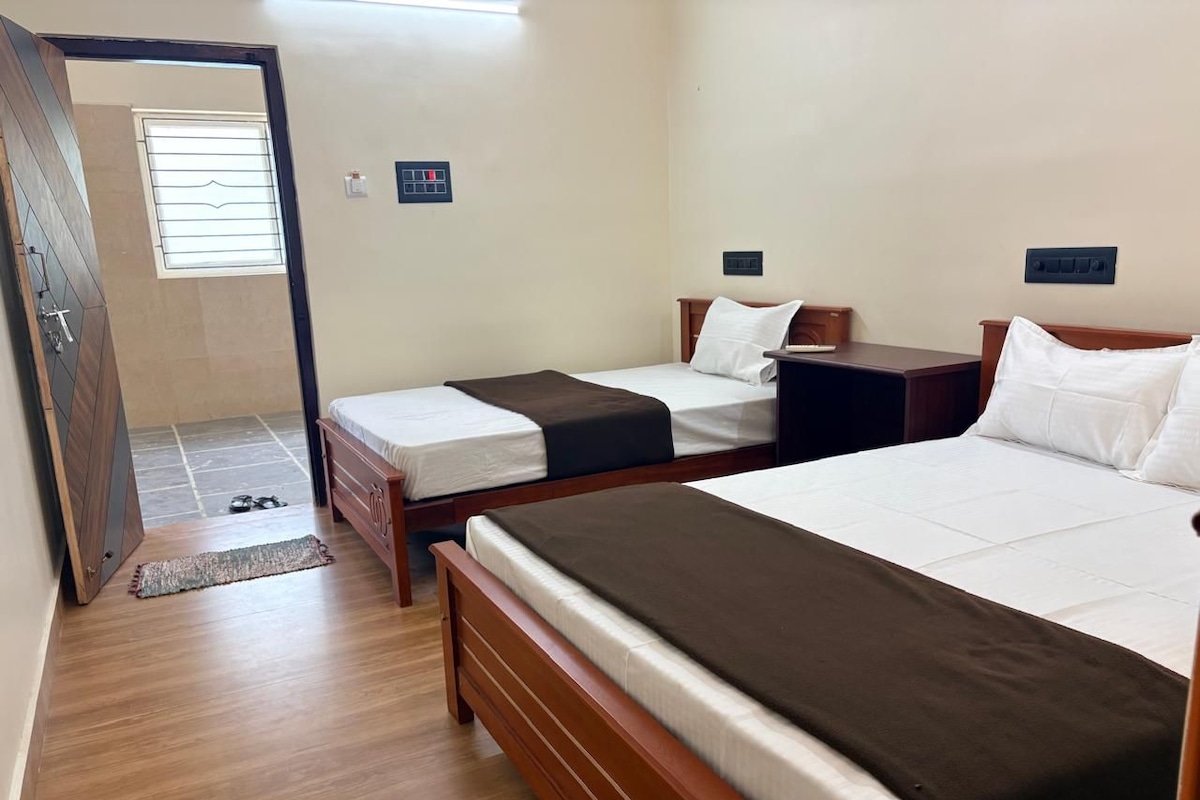 Quarto de hotel com duas camas de solteiro, um guarda-roupa de madeira, uma mesa pequena e uma janela com persianas.