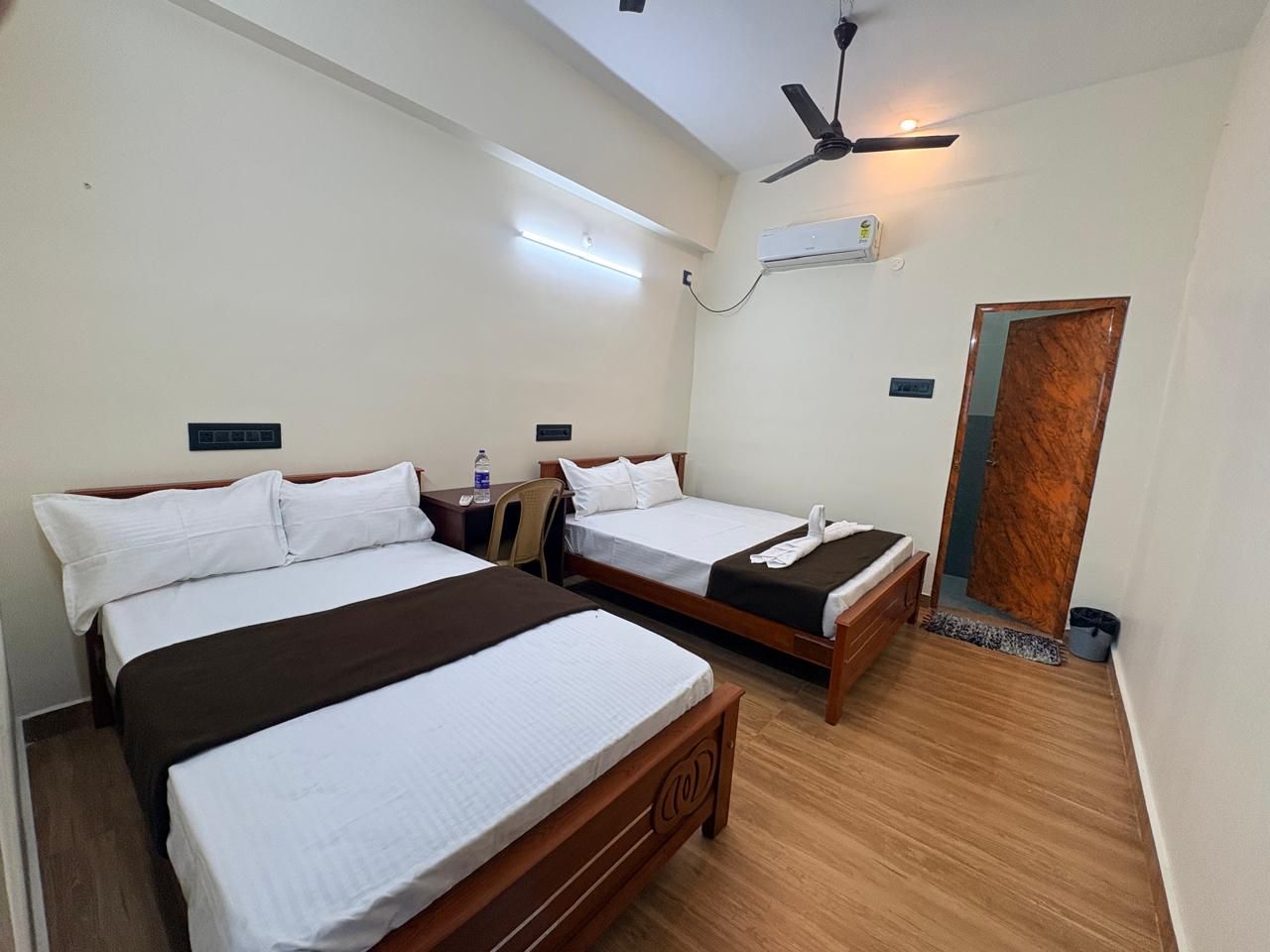 Habitación de hotel con dos camas, un ventilador de techo, un equipo de aire acondicionado y una puerta de madera.