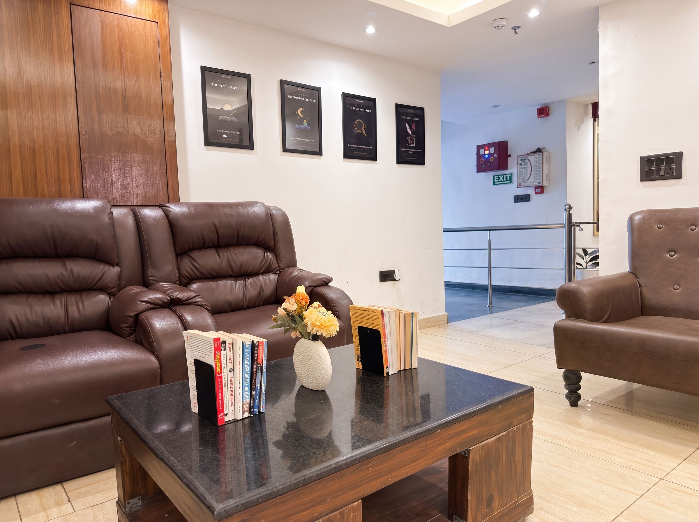 A modern lounge area with leather sofas, a coffee table with books and a vase of flowers, and framed artwork on the wall.