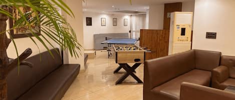 A modern living room with a foosball table, sofas, and a large plant.