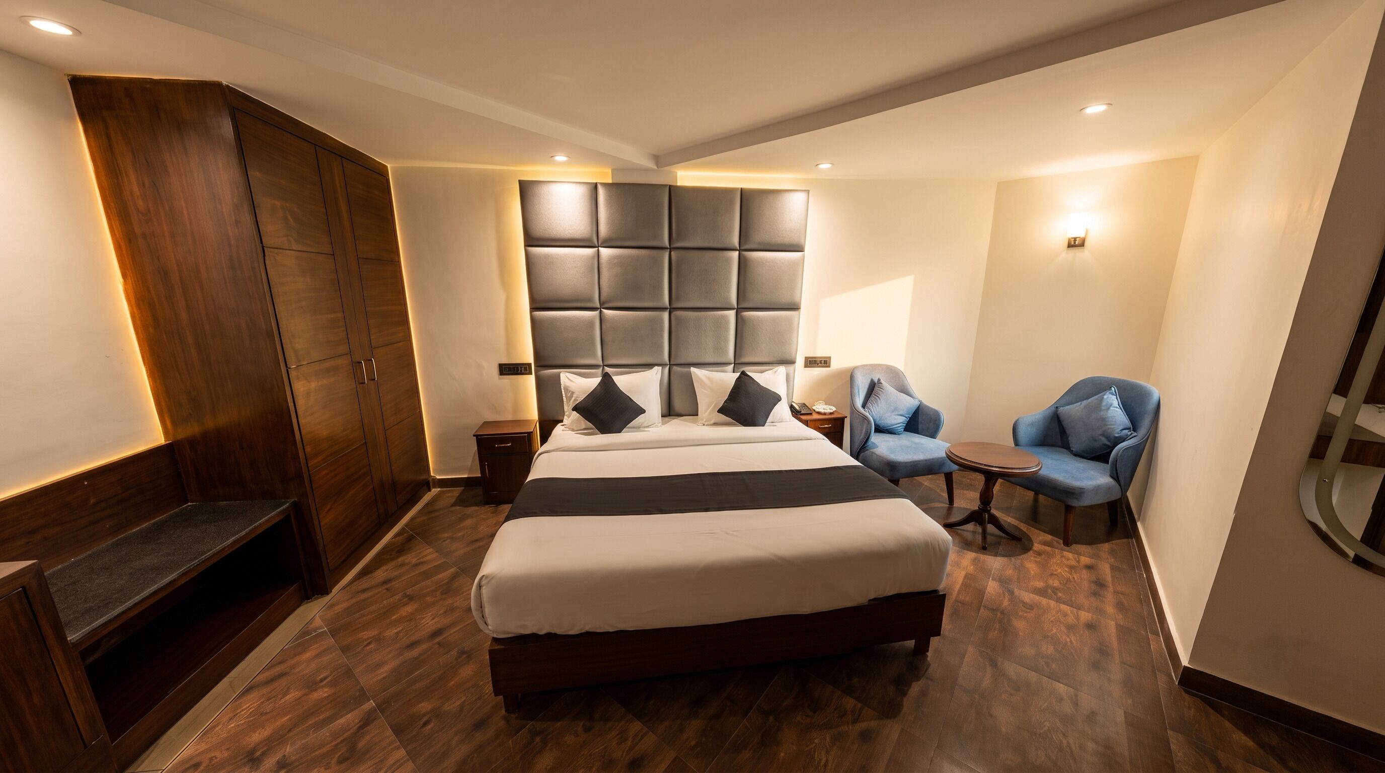 Una habitació d'hotel amb un llit gran, un armari, una zona de seients amb dues cadires i una taula petita.