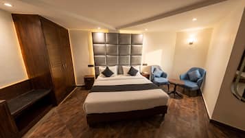 Una habitació d'hotel amb un llit gran, un armari, una zona de seients amb dues cadires i una taula petita.