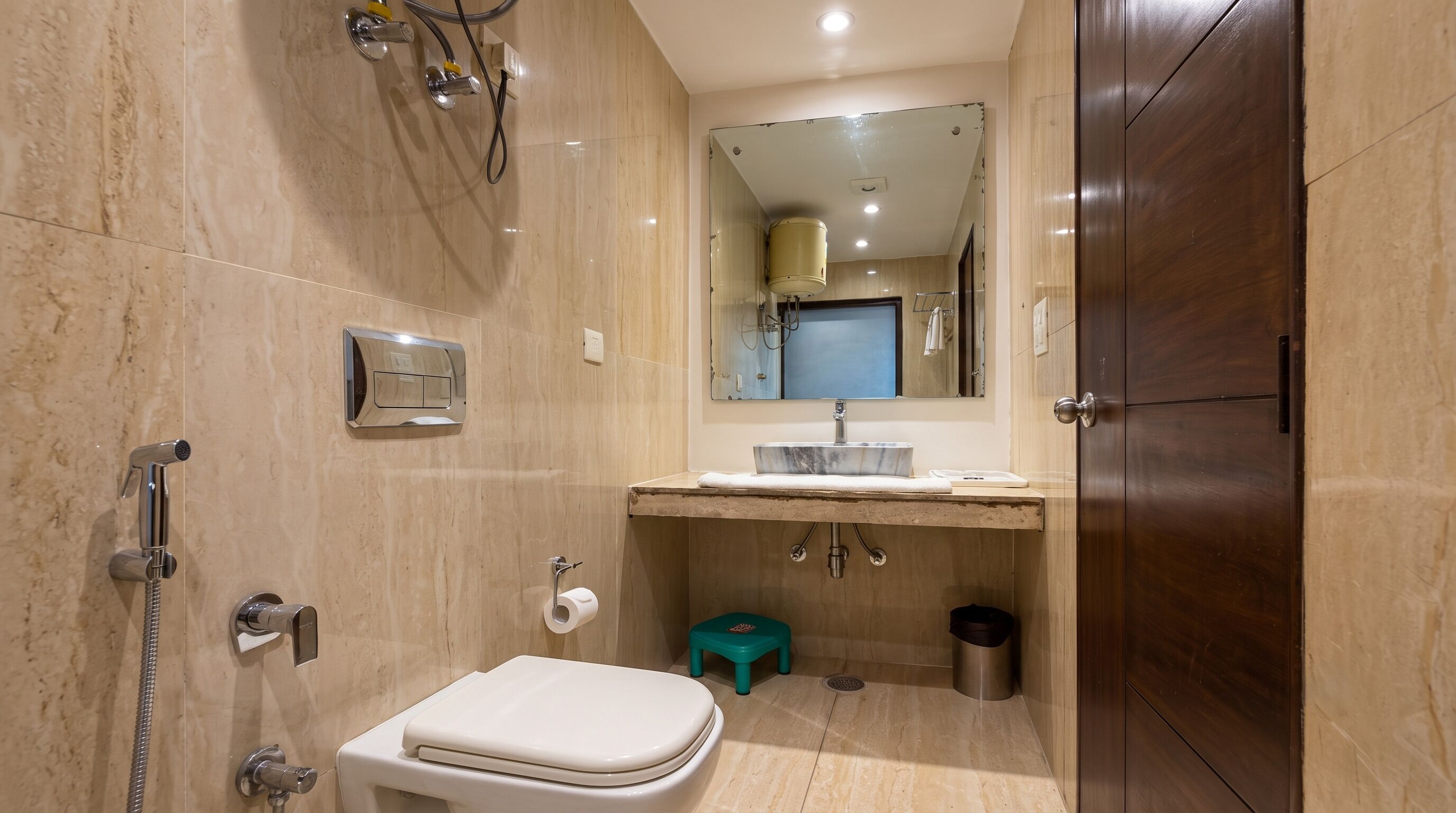 Un bagno con toilette, lavandino, specchio, doccia e uno sgabello.