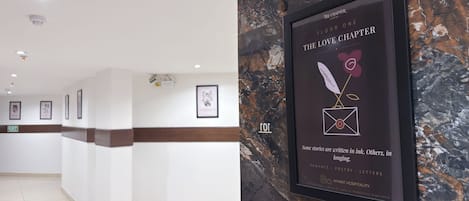 A hotel reception area with a marble wall, framed artwork, and a sign indicating the hotel's name and location.