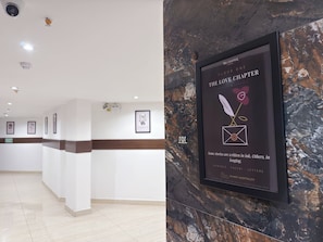 Zona de recepción de hotel con pared de mármol, obras de arte enmarcadas y un cartel con el nombre y la ubicación del hotel.