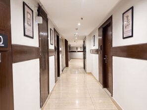 Un pasillo de hotel con puertas de madera, cuadros enmarcados y piso de baldosas.
