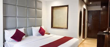 A hotel room with a large bed, a grey headboard, a wooden door, and a framed artwork on the wall.