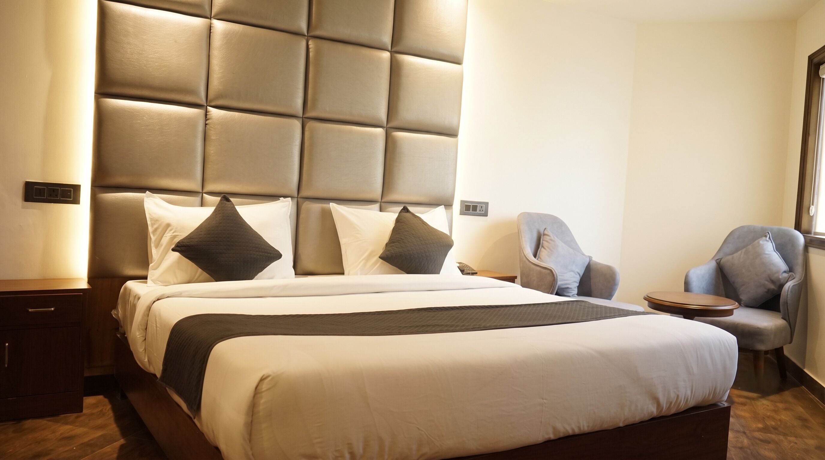 A hotel room with a large bed, a padded headboard, a bedside table, a chair, and a nightstand.
