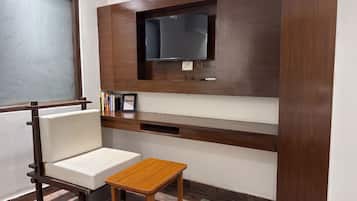 A room with a built-in TV, a white cushioned chair, a small wooden table, and a grey rug.
