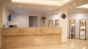 A reception desk with a flat-screen TV, a vase with flowers, and a wall-mounted air conditioning unit.