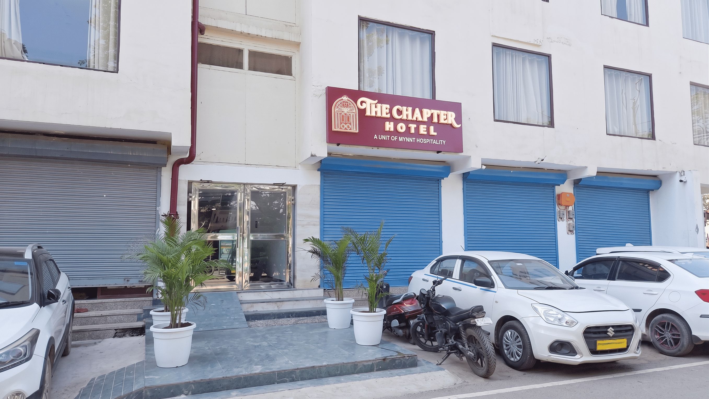 Un hotel con un letrero color borgoña, persianas cerradas y coches estacionados.