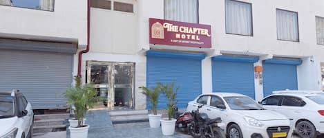 A hotel with a maroon sign, closed shutters, and parked cars.