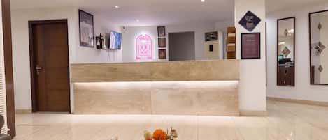 A hotel reception area with a reception desk, framed artwork, a digital display, and a floral arrangement.