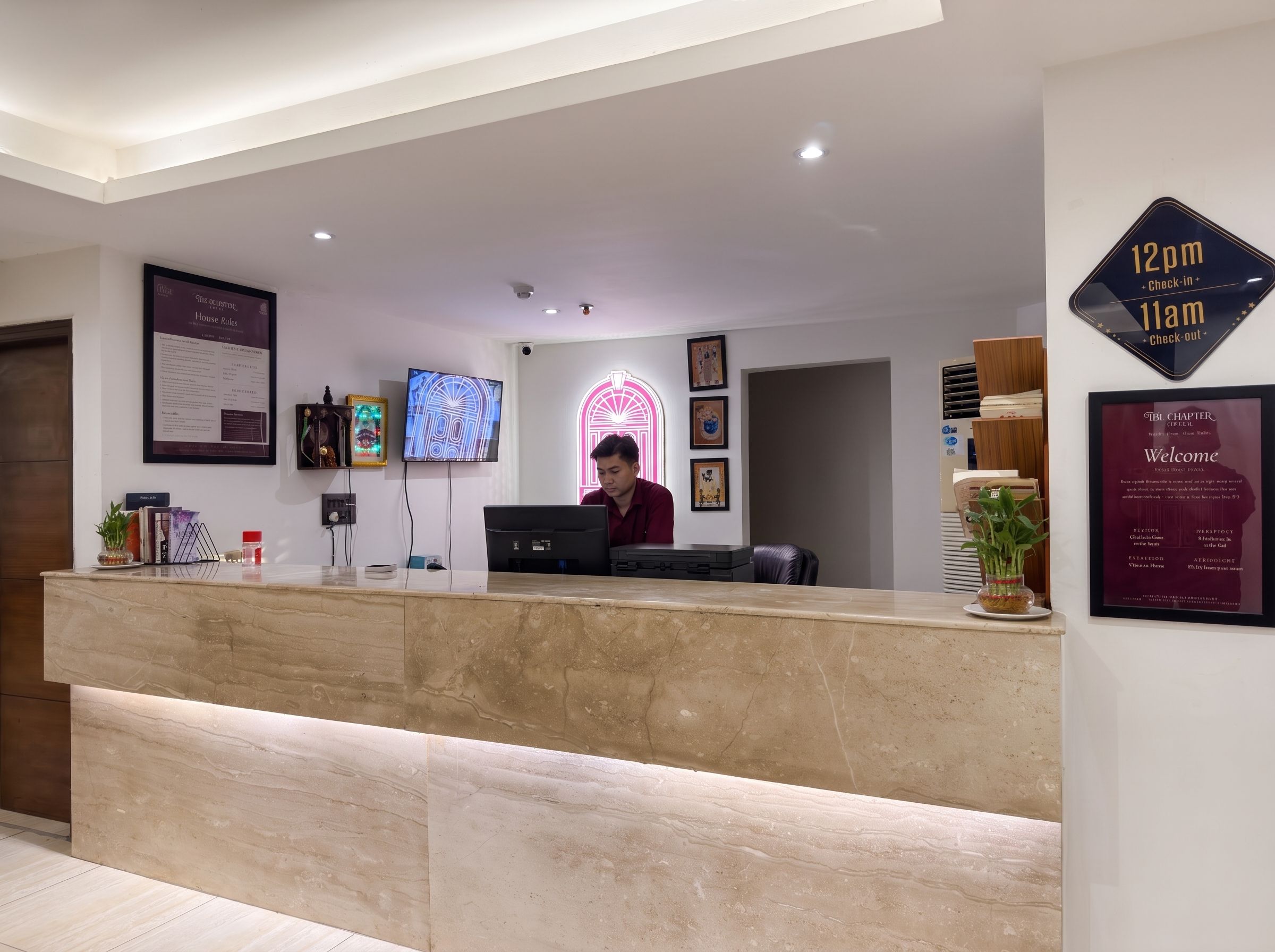 Zona de recepción de un hotel con mostrador de mármol, pantalla digital y letrero de neón.