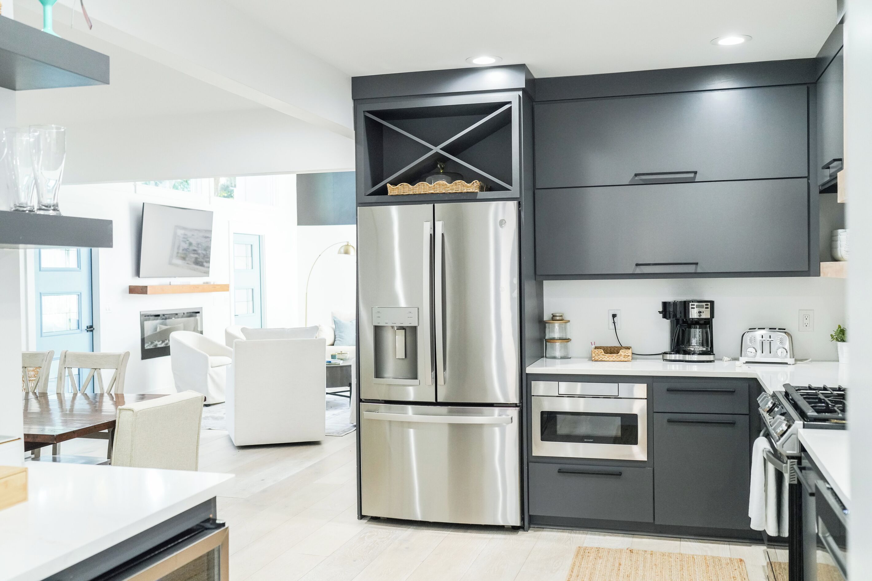 A modern kitchen with stainless steel appliances, grey cabinetry, and a dining area with white furniture.