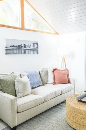Ein Wohnzimmer mit einem hellen Sofa, einem schwarzen und weißen Foto im Rahmen an der Wand und einem Staffelei aus Holz.