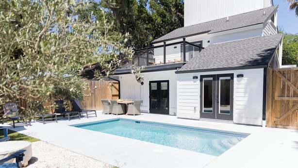 A modern house with a swimming pool, a covered patio, and a wooden fence. - Fall Special! Newly updated large home with pool! (St Simons Island)