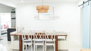 A dining area with a wooden table and white chairs, a woven pendant light, and a sliding barn door. - Fall Special! Newly updated large home with pool! (St Simons Island)