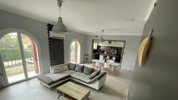 A modern living room with a sectional sofa, a dining area, and a kitchen in the background. - 4-Bedroom Apartment, 130 m², for Rehabilitation/Vacation Use (Balaruc-le-Vieux)