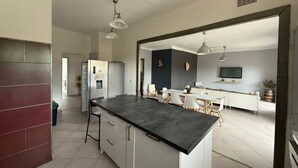 A modern kitchen with a central island, a dining area with a table and chairs, and a living space with a sofa and TV. - 4-Bedroom Apartment, 130 m², for Rehabilitation/Vacation Use (Balaruc-le-Vieux)
