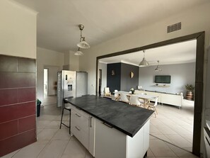 A modern kitchen with a central island, a dining area with a table and chairs, and a living space with a sofa and TV. - 4-Bedroom Apartment, 130 m², for Rehabilitation/Vacation Use (Balaruc-le-Vieux)