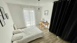 A bedroom with a bed, a desk with a laptop, a chair, a small table with a lamp, and a window with curtains. - 4-Bedroom Apartment, 130 m², for Rehabilitation/Vacation Use (Balaruc-le-Vieux)