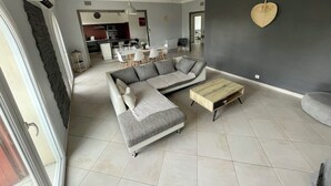 A modern living room with a sectional sofa, a wooden coffee table, and a dining area in the background. - 4-Bedroom Apartment, 130 m², for Rehabilitation/Vacation Use (Balaruc-le-Vieux)