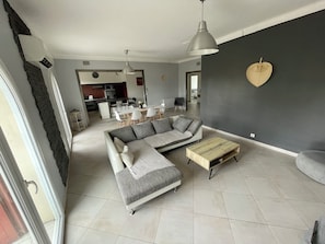 A modern living room with a sectional sofa, a wooden coffee table, and a dining area in the background. - 4-Bedroom Apartment, 130 m², for Rehabilitation/Vacation Use (Balaruc-le-Vieux)