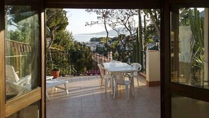 Uma varanda com mesa e cadeiras, vista para o mar e um vaso de planta.