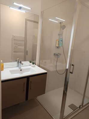 A bathroom with a glass-enclosed shower, a white sink with a mirror above it, and a towel rack. - T2 Cosy Groupama Stadium LDLC Arena (Décines-Charpieu)