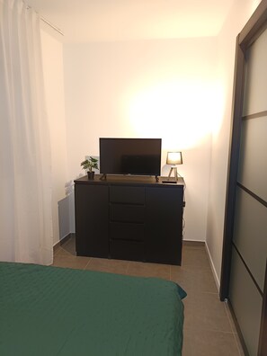 A room with a bed, a TV on a cabinet, a lamp, and a plant. - T2 Cosy Groupama Stadium LDLC Arena (Décines-Charpieu)