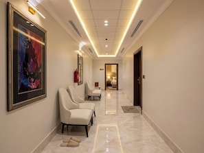 A hotel hallway with a reception desk, a framed abstract painting, and a row of seating areas.