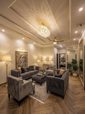 A modern living room with a sectional sofa, armchairs, a coffee table, and a chandelier. - Regency Suite Hotel (lahore)