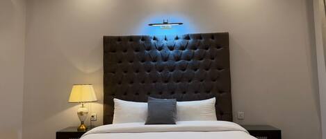 A hotel room with a large bed, a dark tufted headboard, a bedside lamp, and a wall-mounted light fixture.