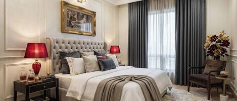 A bedroom with a large bed, two bedside tables with lamps, a chair, a painting on the wall, and a window with curtains.