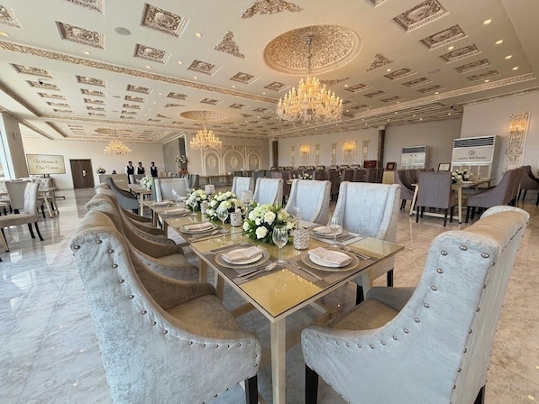 A formal dining room with a long table set for a banquet, elegant chairs, and a chandelier.