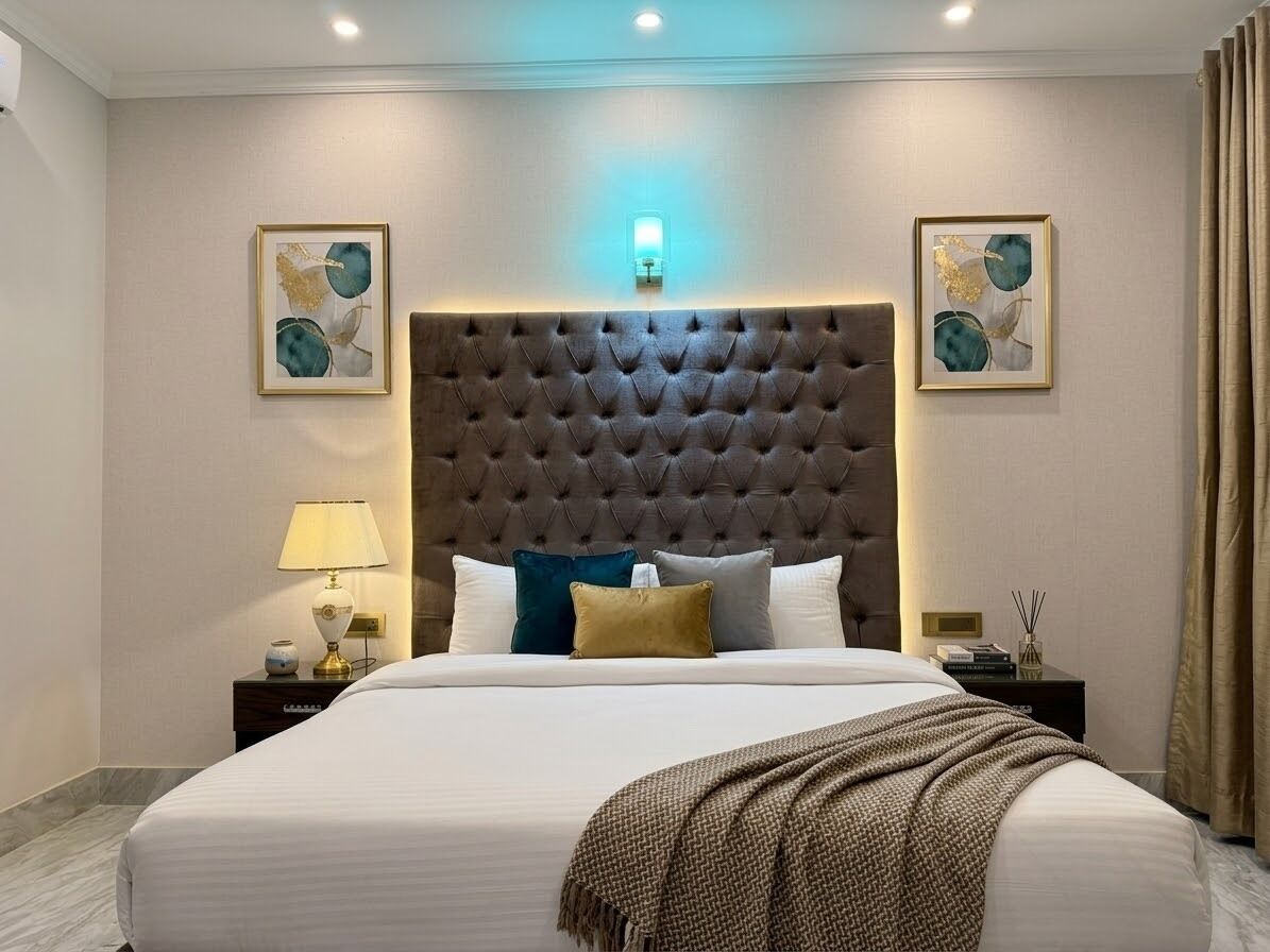 Ein Hotelzimmer mit einem großen Bett, einem gepolsterten Kopfteil, zwei Nachttischen mit Lampen und Kunstwerken an den Wänden.